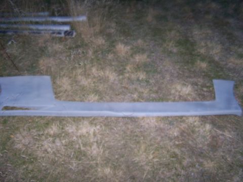 1994 Ford Probe - A car side skirt part is shown lying on the ground outdoors.