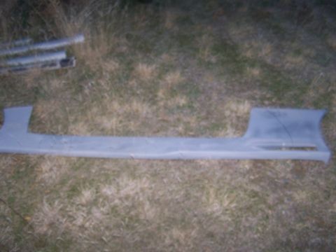 1994 Ford Probe - A single car part, a side skirt, is shown resting on the ground outdoors.