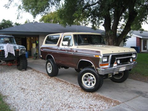 1979 Ford Bronco - A lifted two-tone Ford Bronco sits in a driveway, with another lifted vehicle to its left.