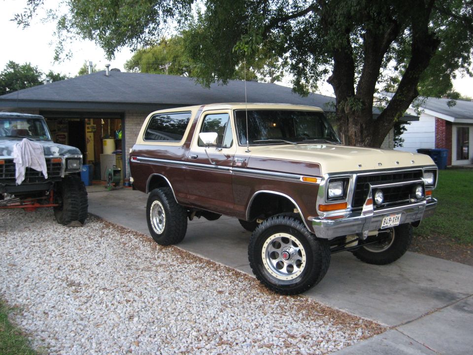 Lifted two-tone brown and tan Ford Bronco parked in a driveway next to another lifted truck