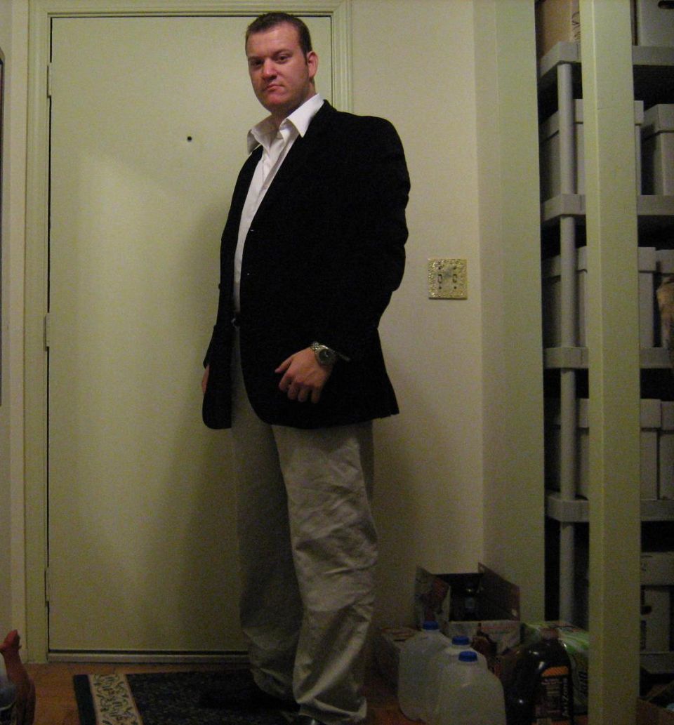 Man in a dark blazer and khaki pants standing by a white door
