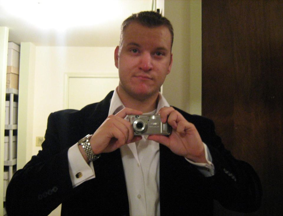 Man in a blazer taking a mirror selfie with a compact camera