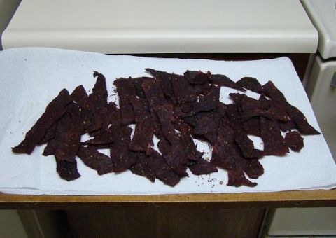 1989 Ford Bronco - Strips of dark peppered homemade beef jerky spread out to cool on a white paper towel on a kitchen counter next to an appliance.