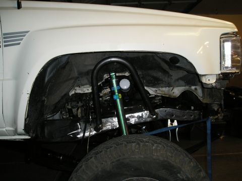 1986 Toyota Hilux - Custom suspension work is visible in the front wheel well of a white truck, a new shock hoop and a green shock absorber.