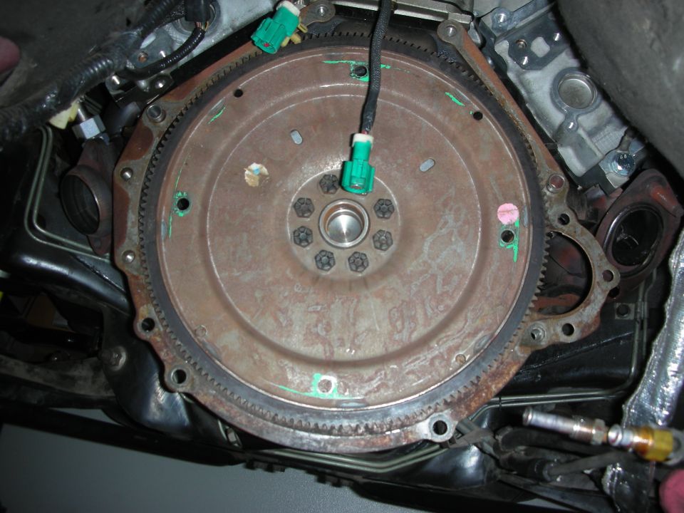 Close-up of a rusty flywheel with a sensor connector attached, part of a vehicle's transmission