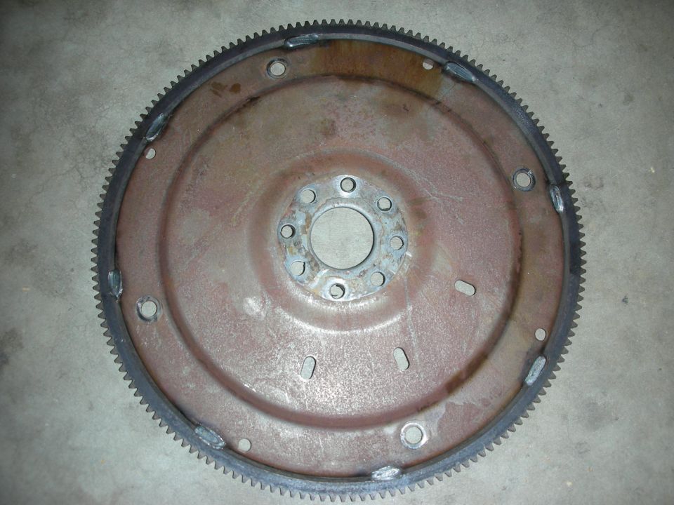 Rusty metal flywheel with a toothed outer edge and a central circular opening with bolt holes