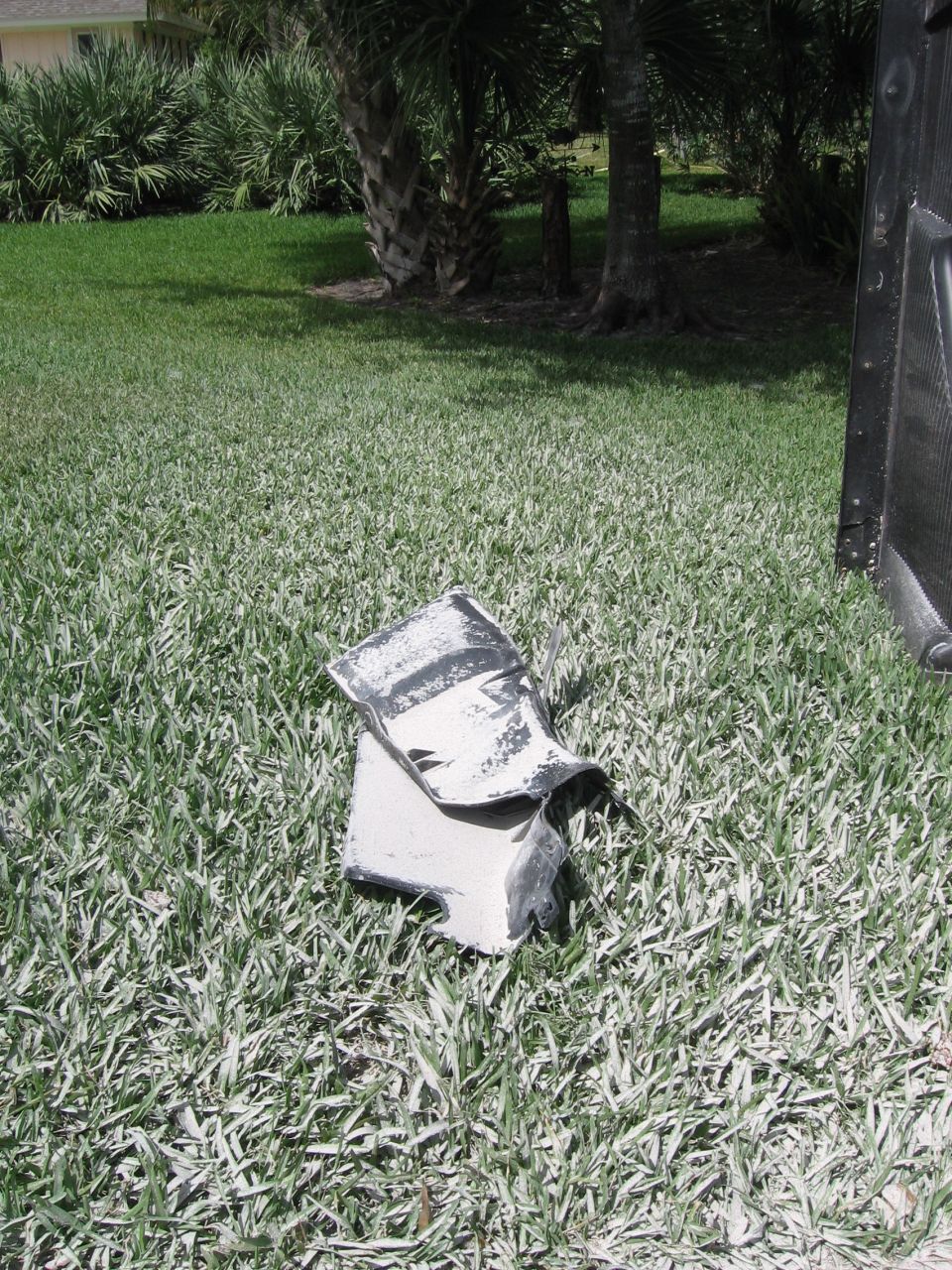 Bent and torn white and black car fender part on grass