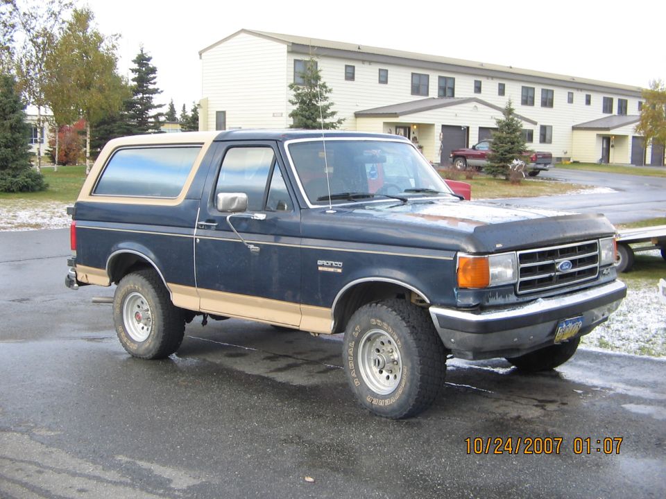 Dark blue Ford Bronco with tan top and trim, parked outside a building
