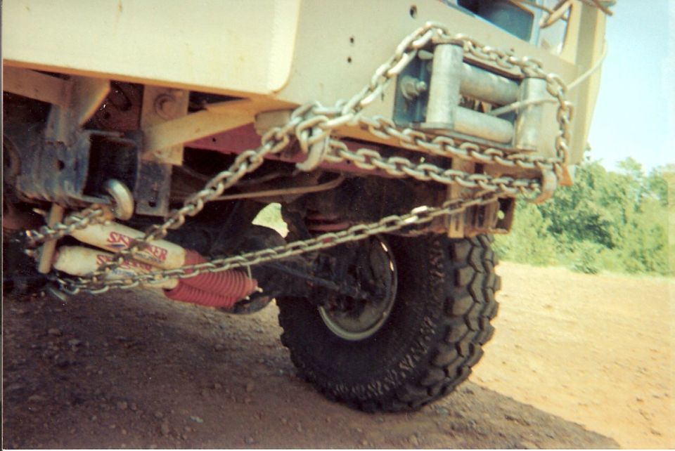 Rear view of a vehicle with a winch and chains attached to the bumper and frame. Red shock absorbers are visible