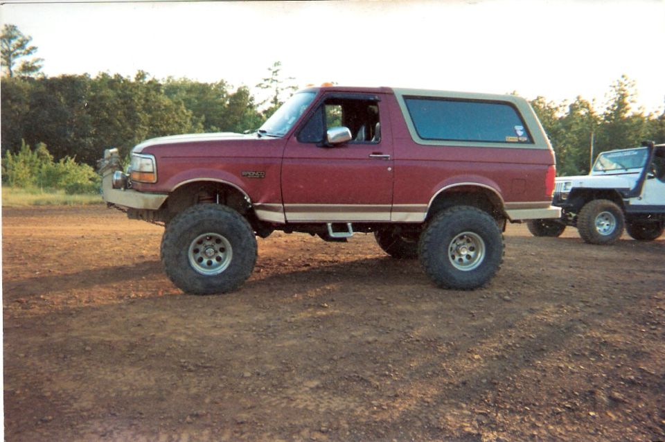 Lifted red Ford Bronco parked on dirt with a white Jeep behind it