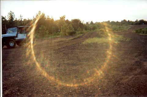 1995 Ford Bronco - A white SUV sits idle on a dirt path, its doors ajar, under a bright sky with a prominent lens flare.
