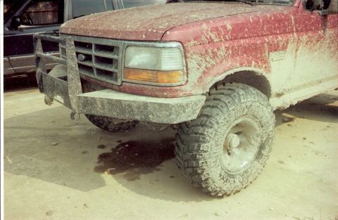 1995 Ford Bronco - This muddy red pickup truck has a heavy-duty brush guard and off-road tires, suggesting it's used for off-roading.