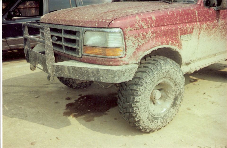 Front end of a red pickup truck covered in mud, with a brush guard and large tires