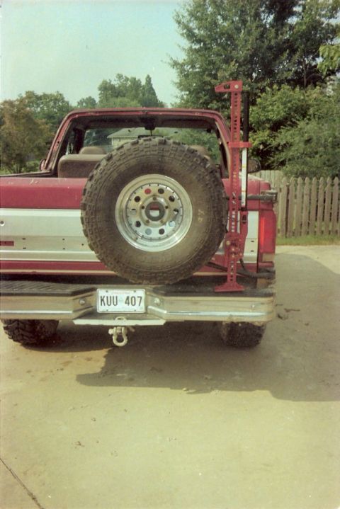 1995 Ford Bronco - Rear view of a red 1995 Ford Bronco equipped with a spare tire and a Hi-Lift jack, ready for off-road adventures.
