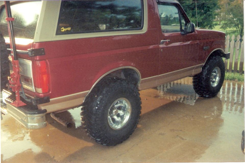 Red Ford Bronco with tan trim and off-road tires, viewed from the rear quarter