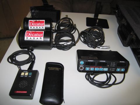 1991 Ford LTD Crown Victoria - A collection of Decatur radar equipment, including two radar units and a control box, is laid out on a table.