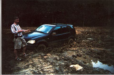 1995 Ford Bronco - A man stands next to a dark SUV that is deeply stuck in mud.