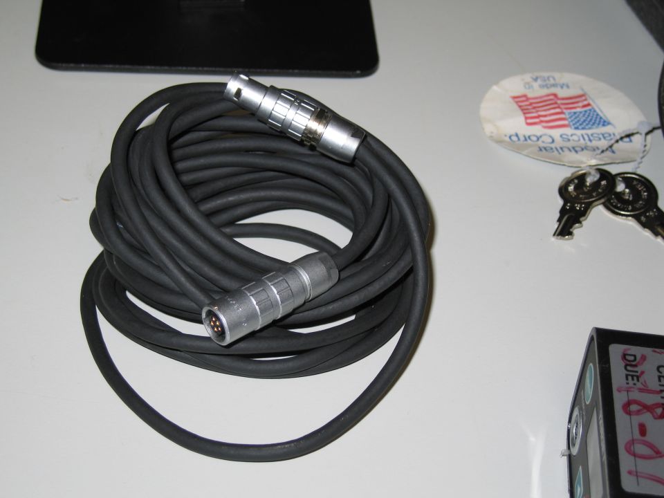 Coiled black audio cable with silver multi-pin connectors on each end. Two keys and a tag are nearby