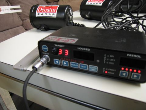 1991 Ford LTD Crown Victoria - Two Decatur radar units and a police radar detector are shown on a table. The detector displays a speed of 33.