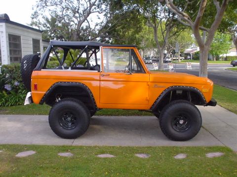 1977 Ford Bronco - Side view of an orange 1977 Ford Bronco with a black soft top and roll cage.