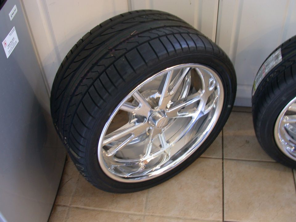 Polished chrome multi-spoke wheel with low-profile tire standing on tile floor indoors