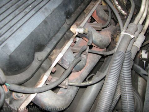 1994 Chevrolet Silverado 3500 - Close-up view of an engine's exhaust manifold and associated wiring, with some text visible on a hose.
