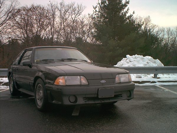 Black Fox-body Ford Mustang GT hatchback parked by a guardrail with snow piled in the background