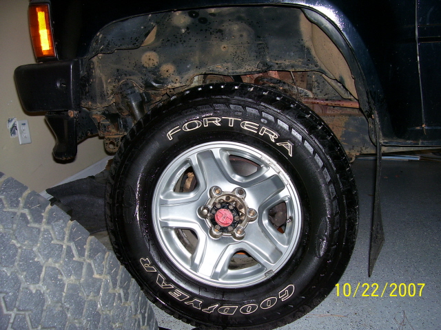 Front wheel and fender well of a dark-colored SUV. Tire has 'FORTERA' and 'GOODYEAR' text