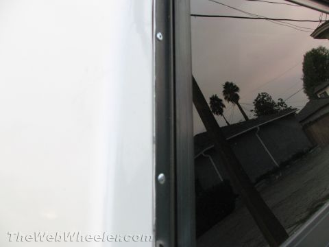 1994 Chevrolet Silverado 3500 - A close-up view of a white trailer's side panel, showing the trim and a reflection of a suburban scene.