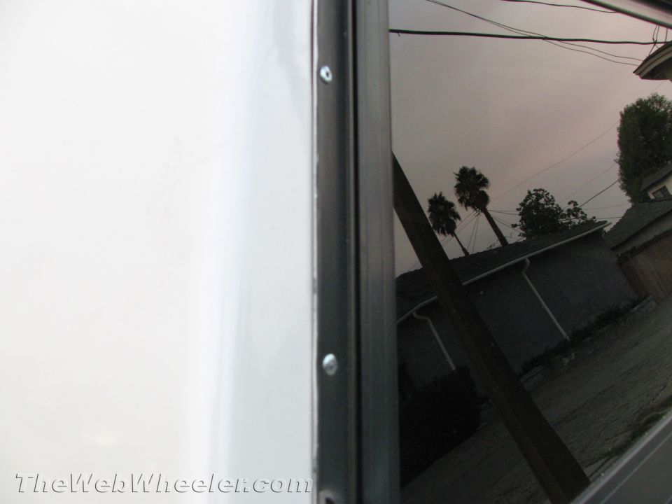 White trailer side panel with black trim and reflection of houses, palm trees, and power lines