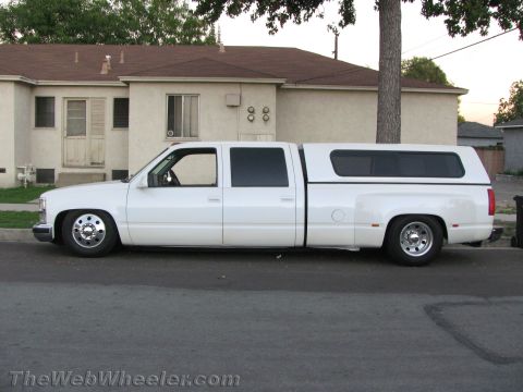 1994 Chevrolet Silverado 3500 - A white lowered Chevrolet crew-cab dually pickup shown in side profile, fitted with a matching white bed camper shell and chrome dual rear…