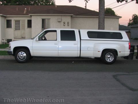 1994 Chevrolet Silverado 3500 - A white 1990s Chevrolet crew-cab dually pickup shown in side profile on a residential street, fitted with a matching camper shell, chrome d…
