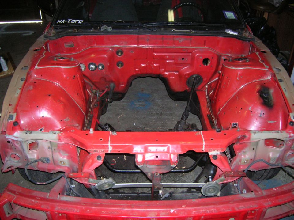 Red car engine bay, missing engine. Some parts removed. Sticker on windshield says HA-Toro