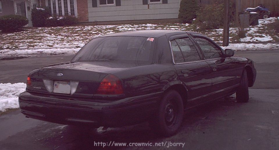 Black Ford Crown Victoria sedan parked on snowy residential street, rear three-quarter view