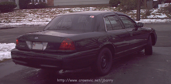 Rear view of black Ford Crown Victoria with red taillights lit, parked in a snowy yard