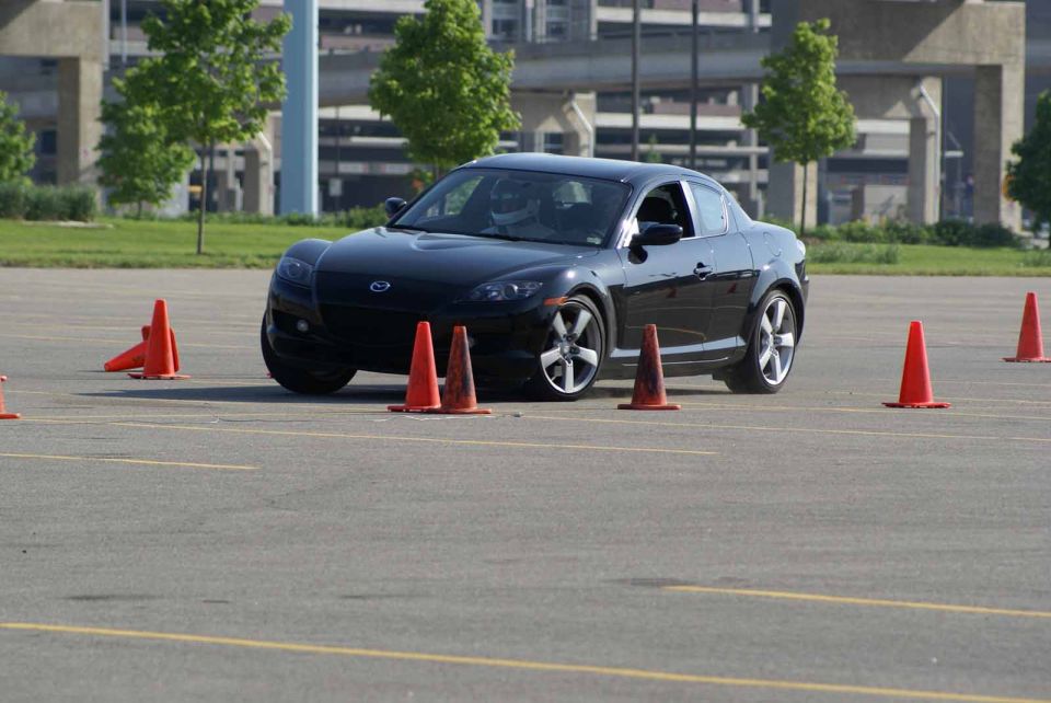 Black coupe with racing cones on asphalt lot