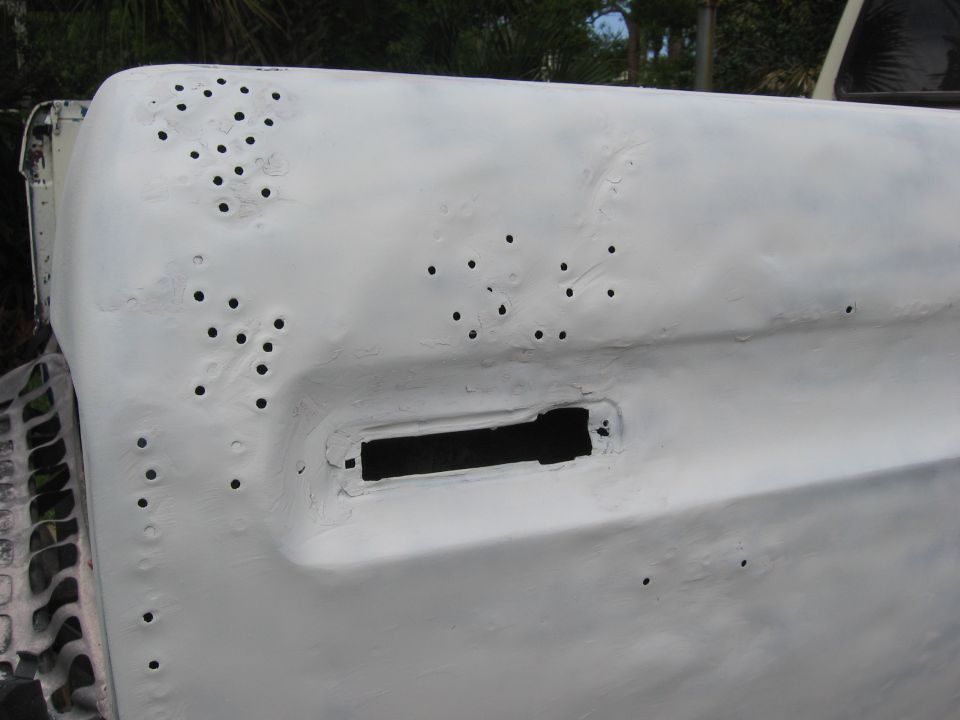 close-up of a white primed vehicle body panel with many small holes and a rectangular cutout