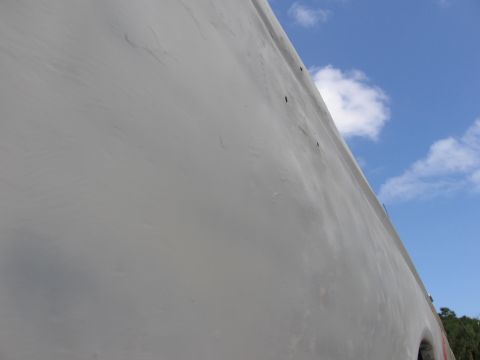 1979 Ford F-150 - Close-up view of a vehicle's side panel, showing texture and a few small holes under a partly cloudy sky.