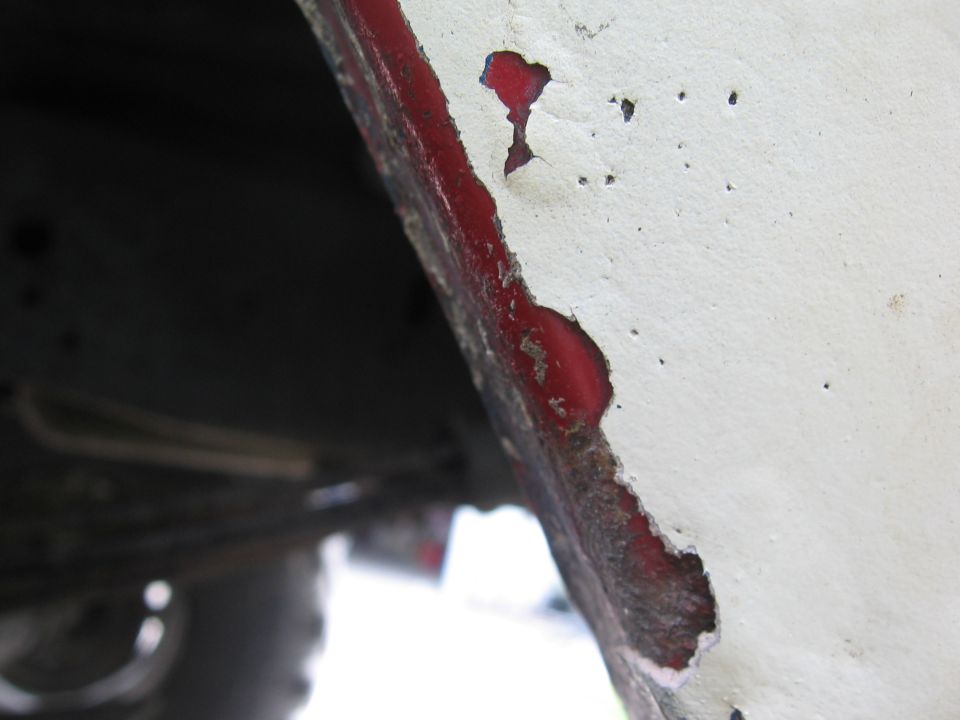 Close-up of a white painted metal edge with red showing through rust and peeling paint, likely a wheel well