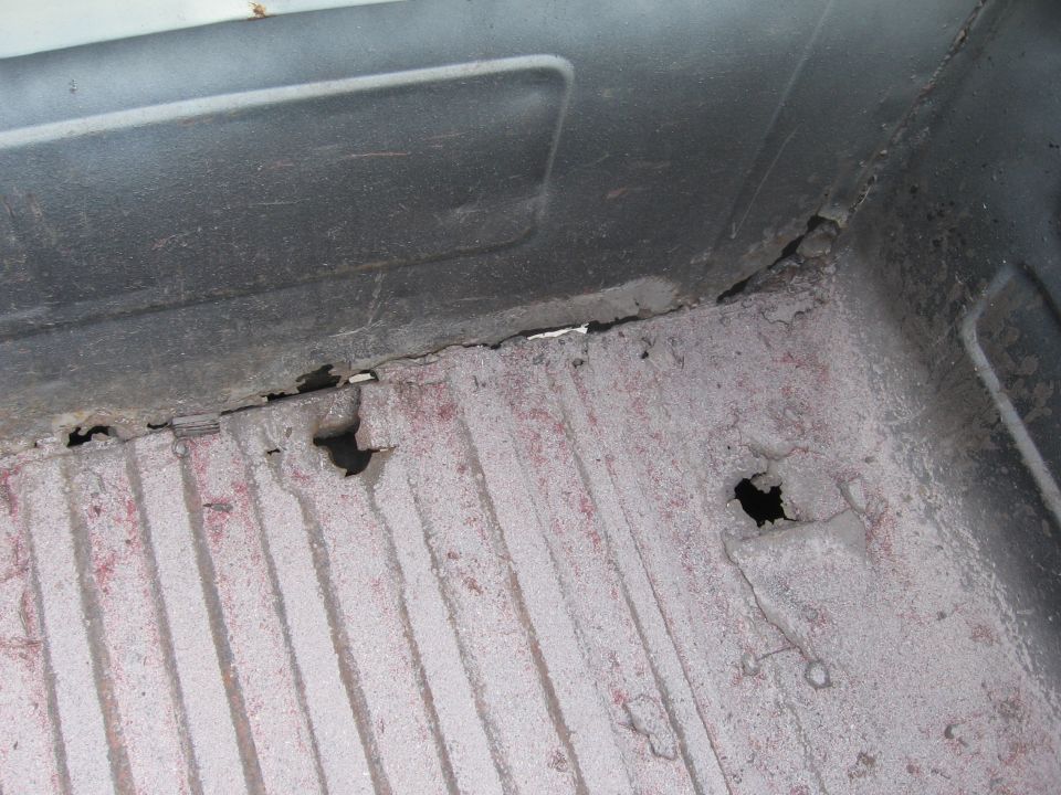 Corroded truck bed floor with holes and red undercoating