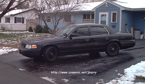 Side profile of black Ford Crown Victoria on black steel wheels in a residential driveway
