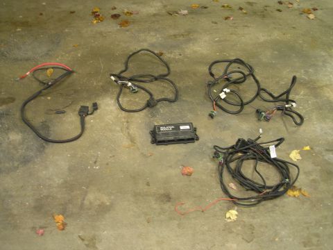 1994 Ford Bronco - Snow plow light wiring harnesses laid out on a stained concrete garage floor scattered with fallen leaves, including a heavy red/black batt…