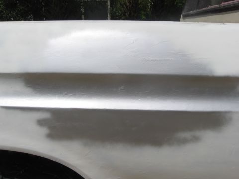 1979 Ford F-150 - Close-up of a white truck fender showing areas of body filler and primer, indicating repair work.
