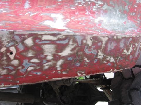 1979 Ford F-150 - Body filler is visible on the lower section of a red vehicle's body panel, indicating repair work.