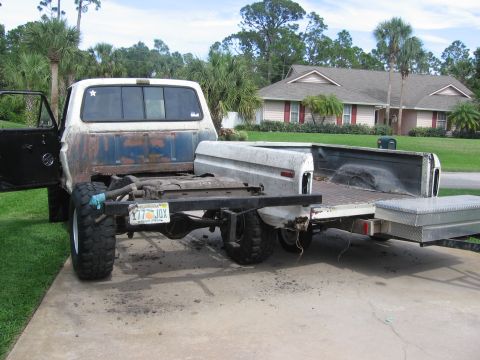 1979 Ford F-150 - A pickup truck chassis is prepared for a cab swap, with a separate truck bed loaded onto a trailer.