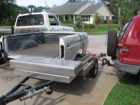 1979 Ford F-150 - A white Ford F-150 truck bed and fender are transported on a trailer pulled by a red SUV.