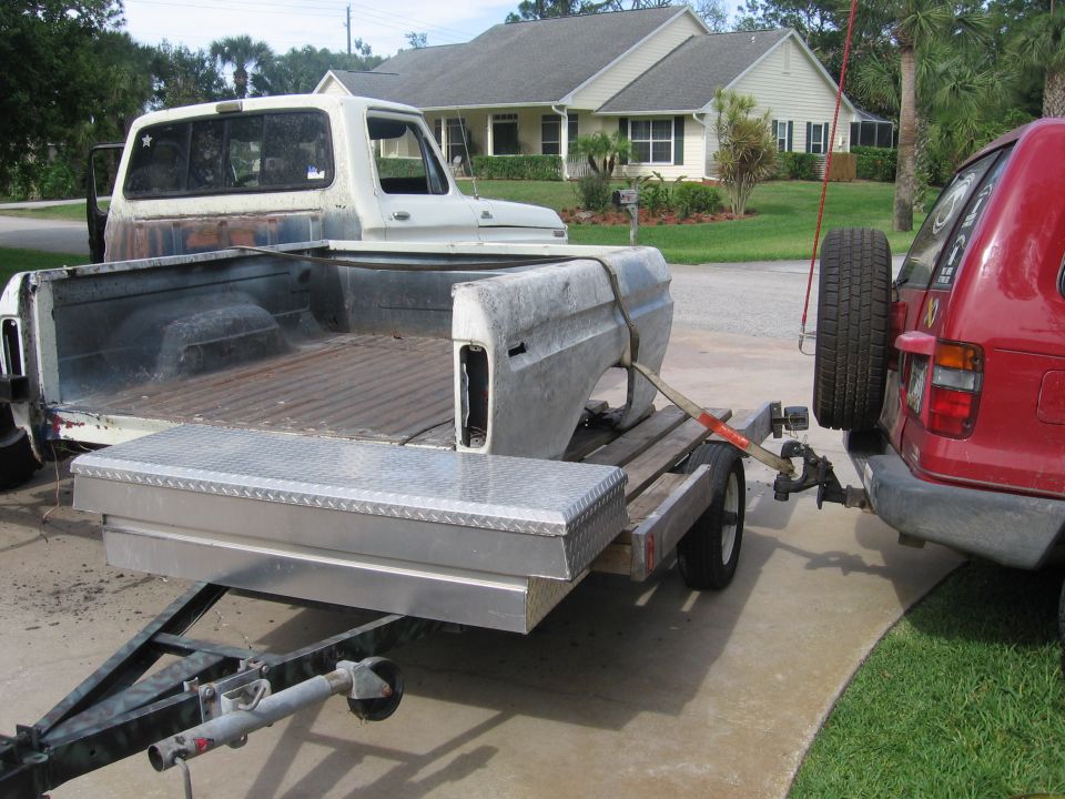 White Ford F-150 truck bed and fender on a trailer towed by a red SUV