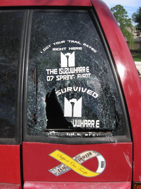 1979 Ford F-150 - The rear window of a red vehicle is cracked and features several stickers, including one referencing an 'Isuzuwharre' event.