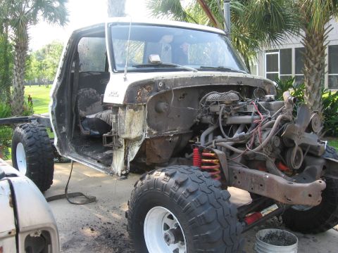 1979 Ford F-150 - Three-quarter front view of a stripped white pickup cab on its frame in a driveway, with the fenders, bed, doors and hood removed to expose…