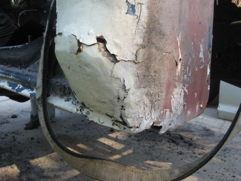 1979 Ford F-150 - Close-up of the lower rear corner of a cab showing severe rust-through and rot at the bottom of the cab panel, with white paint flaking awa…